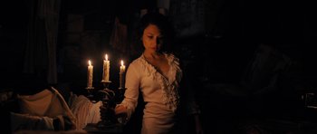 Movie still from “The Duke of Burgundy” (2014), directed by Peter Strickland – A woman in a white shirt is holding a candle; Medium shot, Low angle