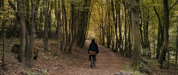 Movie still from “The Duke of Burgundy” (2014), directed by Peter Strickland – A person riding a bike down a trail in the woods; Extreme Wide shot, High angle
