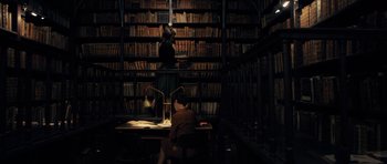 Movie still from “The Duke of Burgundy” (2014), directed by Peter Strickland – A person sitting at a table in a library; Wide shot, High angle