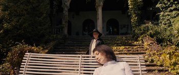 Movie still from “The Duke of Burgundy” (2014), directed by Peter Strickland – Two people sitting on a bench in front of a building; Wide shot, High angle
