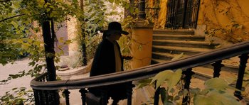 Movie still from “The Duke of Burgundy” (2014), directed by Peter Strickland – A man in a hat and a cape walking down a staircase; Wide shot, High angle