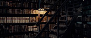 Movie still from “The Duke of Burgundy” (2014), directed by Peter Strickland – A room filled with lots of books and stairs; Wide shot, High angle