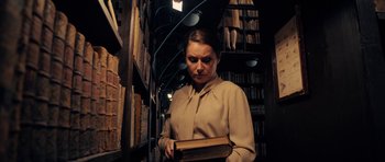 Movie still from “The Duke of Burgundy” (2014), directed by Peter Strickland – A woman holding an open book in a library; Medium shot, Low angle