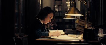 Movie still from “The Duke of Burgundy” (2014), directed by Peter Strickland – A woman sitting at a table writing on a piece of paper; Medium shot, Low angle
