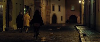 Movie still from “The Duke of Burgundy” (2014), directed by Peter Strickland – A person riding a bike on a street at night; Wide shot, Over the shoulder angle