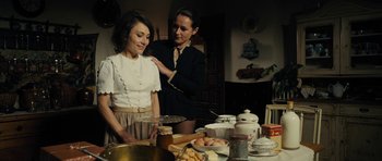 Movie still from “The Duke of Burgundy” (2014), directed by Peter Strickland – Two women standing in front of a table filled with plates of food; Medium shot, Over the shoulder angle