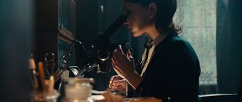 Movie still from “The Duke of Burgundy” (2014), directed by Peter Strickland – A woman looking through a microscope in a dark room; Medium shot, Over the shoulder angle