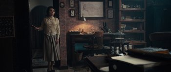 Movie still from “The Duke of Burgundy” (2014), directed by Peter Strickland – A woman standing in front of a desk in a room; Wide shot, High angle