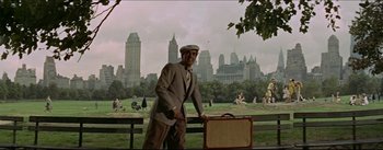 Movie still from “The Eddy Duchin Story” (1956), directed by George Sidney – A man in a suit and hat holding a suit case; Wide shot, Low angle