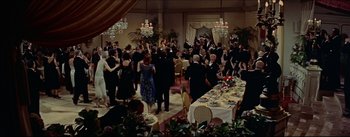 Movie still from “The Eddy Duchin Story” (1956), directed by George Sidney – A large group of people in formal wear standing around a table; Extreme Wide shot, High angle