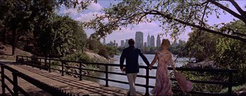 Movie still from “The Eddy Duchin Story” (1956), directed by George Sidney – A man and a woman holding hands while standing next to a river; Wide shot, High angle