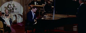 Movie still from “The Eddy Duchin Story” (1956), directed by George Sidney – A man sitting at a grand piano in front of a group of people; Medium shot, High angle