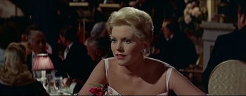 Movie still from “The Eddy Duchin Story” (1956), directed by George Sidney – A woman in a white dress sitting at a table with a flower; Close Up shot, Over the shoulder angle