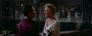 Movie still from “The Eddy Duchin Story” (1956), directed by George Sidney – A man and a woman standing next to each other in front of a city skyline at night; Medium shot, Over the shoulder angle