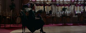 Movie still from “The Eddy Duchin Story” (1956), directed by George Sidney – A woman sitting on a chair in a room; Wide shot, Over the shoulder angle