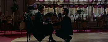 Movie still from “The Eddy Duchin Story” (1956), directed by George Sidney – A man kneeling down next to a woman in high heels; Wide shot, Low angle