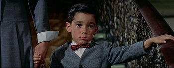 Movie still from “The Eddy Duchin Story” (1956), directed by George Sidney – A young boy wearing a red bow tie and a gray jacket; Medium shot, High angle
