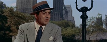 Movie still from “The Eddy Duchin Story” (1956), directed by George Sidney – A man wearing a suit and a hat in a city; Medium shot, Over the shoulder angle