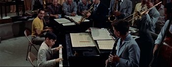 Movie still from “The Eddy Duchin Story” (1956), directed by George Sidney – A group of people sitting around a table with musical instruments on it; Medium shot, High angle