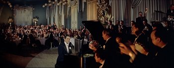 Movie still from “The Eddy Duchin Story” (1956), directed by George Sidney – A man sitting at a piano in front of an audience; Wide shot, High angle