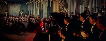Movie still from “The Eddy Duchin Story” (1956), directed by George Sidney – A group of people sitting in a room with musical instruments; Wide shot, High angle