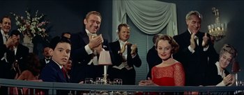 Movie still from “The Eddy Duchin Story” (1956), directed by George Sidney – A group of men and women clapping at a party; Medium shot, Low angle
