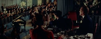 Movie still from “The Eddy Duchin Story” (1956), directed by George Sidney – A man and woman sitting at a table in front of an audience; Wide shot, High angle