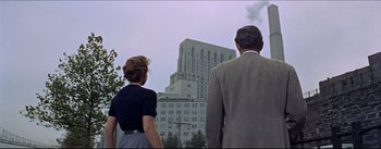 Movie still from “The Eddy Duchin Story” (1956), directed by George Sidney – A man and a woman standing in front of a tall building; Wide shot, Low angle