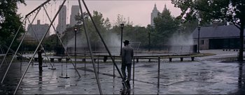 Movie still from “The Eddy Duchin Story” (1956), directed by George Sidney – A man in a hat and a suit is standing in the rain near a fence; Wide shot, High angle