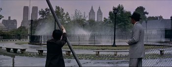 Movie still from “The Eddy Duchin Story” (1956), directed by George Sidney – A man standing in front of a fence and a building; Wide shot, Over the shoulder angle