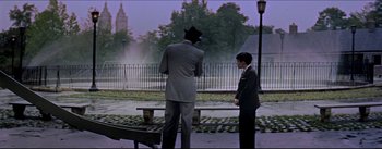 Movie still from “The Eddy Duchin Story” (1956), directed by George Sidney – Two men in suits standing next to each other on a park bench; Wide shot, Over the shoulder angle