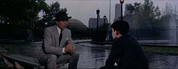Movie still from “The Eddy Duchin Story” (1956), directed by George Sidney – A man in a suit talking to a boy in a suit; Medium shot, Over the shoulder angle