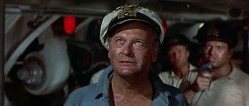 An older man wearing a captain's hat and a blue shirt