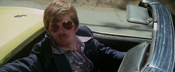 Movie still from “The Enforcer” (1976), directed by James Fargo – A man with a beard and sunglasses sitting in the back of a car; Close Up shot, Low angle