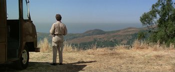 Movie still from “The Enforcer” (1976), directed by James Fargo – A man standing on top of a dry grass field; Extreme Wide shot, Over the shoulder angle