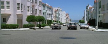 Movie still from “The Enforcer” (1976), directed by James Fargo – Cars parked on the side of the street in a row of houses; Wide shot, Low angle
