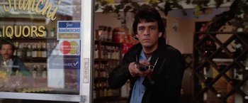Movie still from “The Enforcer” (1976), directed by James Fargo – A man in a black jacket holding a gun in front of a store; Medium shot, Low angle