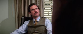 Movie still from “The Enforcer” (1976), directed by James Fargo – A man sitting in a chair wearing a vest and a tie; Close Up shot, Over the shoulder angle