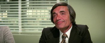 Movie still from “The Enforcer” (1976), directed by James Fargo – A man in a suit and tie sitting in front of a window; Close Up shot, High angle