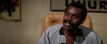 Movie still from “The Enforcer” (1976), directed by James Fargo – A man sitting in an office chair with a mustache; Close Up shot, Low angle