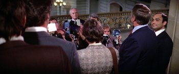 Movie still from “The Enforcer” (1976), directed by James Fargo – A group of people standing in a room taking pictures with cameras; Medium shot, Over the shoulder angle
