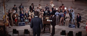 Movie still from “The Enforcer” (1976), directed by James Fargo – A group of people taking pictures of a man in a suit; Wide shot, High angle