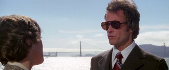 Movie still from “The Enforcer” (1976), directed by James Fargo – A man in a suit and sunglasses standing in front of a body of water; Close Up shot, Over the shoulder angle