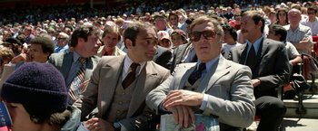 Movie still from “The Enforcer” (1976), directed by James Fargo – Two men in suits are sitting in a crowd of people; Medium shot, High angle
