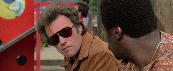 Movie still from “The Enforcer” (1976), directed by James Fargo – A man wearing sunglasses and a brown jacket; Close Up shot, Over the shoulder angle