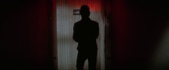 Movie still from “The Enforcer” (1976), directed by James Fargo – A man standing in front of a window with red lights; Wide shot, Low angle