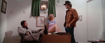 Movie still from “The Enforcer” (1976), directed by James Fargo – A man and a woman sitting on top of a wooden box; Wide shot, Low angle