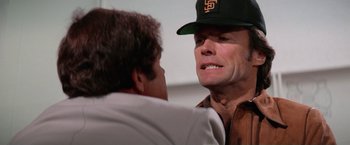 Movie still from “The Enforcer” (1976), directed by James Fargo – A man wearing a baseball cap talking to another man; Close Up shot, Over the shoulder angle