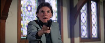 Movie still from “The Enforcer” (1976), directed by James Fargo – A woman holding a gun in front of a stained glass window; Close Up shot, Low angle