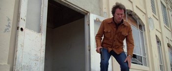 Movie still from “The Enforcer” (1976), directed by James Fargo – A man holding a gun while standing in front of a building; Medium shot, Low angle